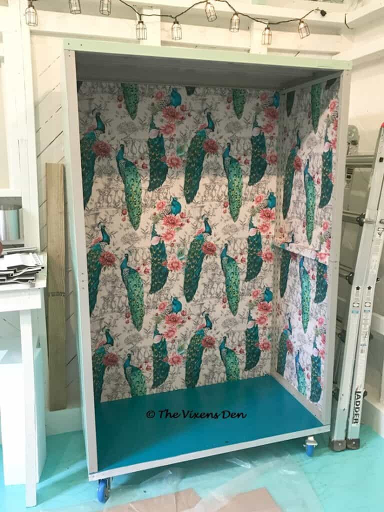 partially assembled metal garage cabinet with painted bottom shelf and back and sides lined with peacock fabric