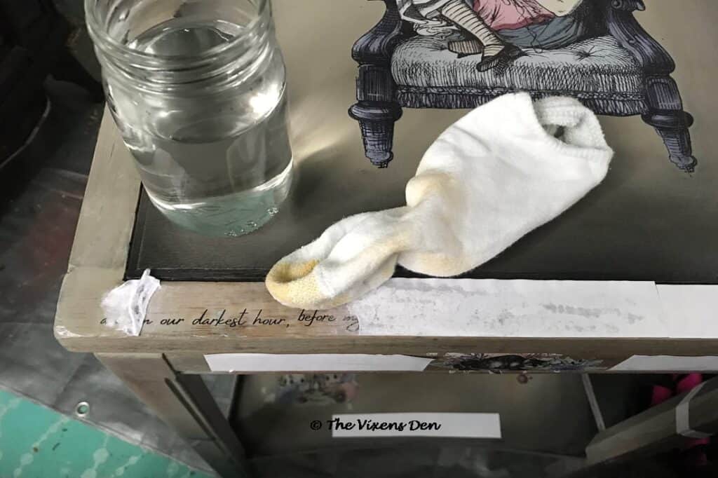 close up of a wet sock and a jar of water sitting on a table top as the paper from a DIY transfer is being rubbed away