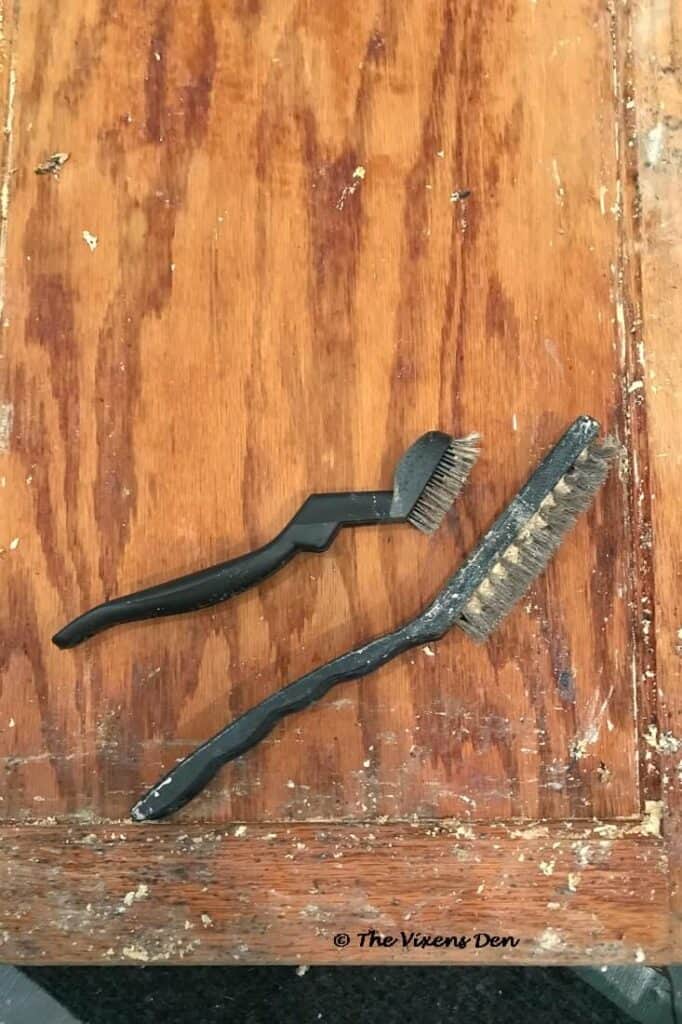 two wire brushes with plastic handles laying on a wood cabinet door that is being stripped