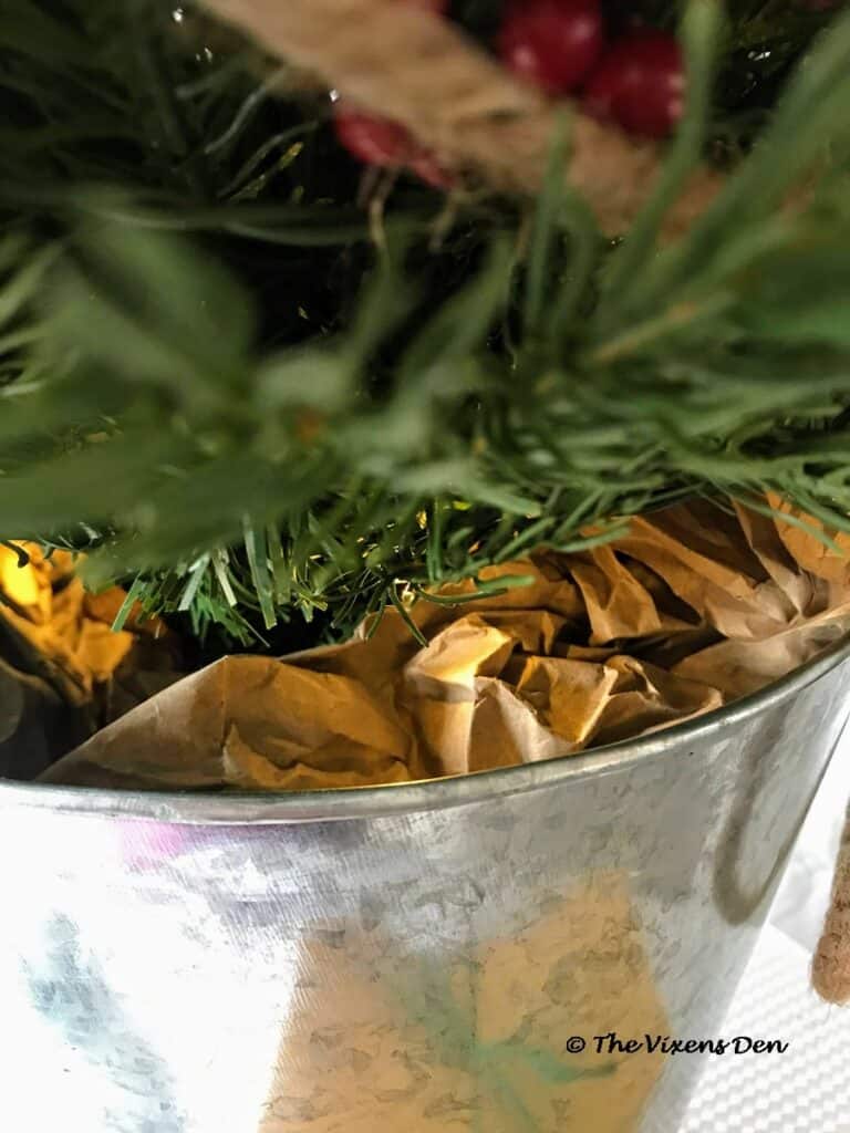 close up of brown paper wrapped around the base of the mini Christmas tree in a metal trash can