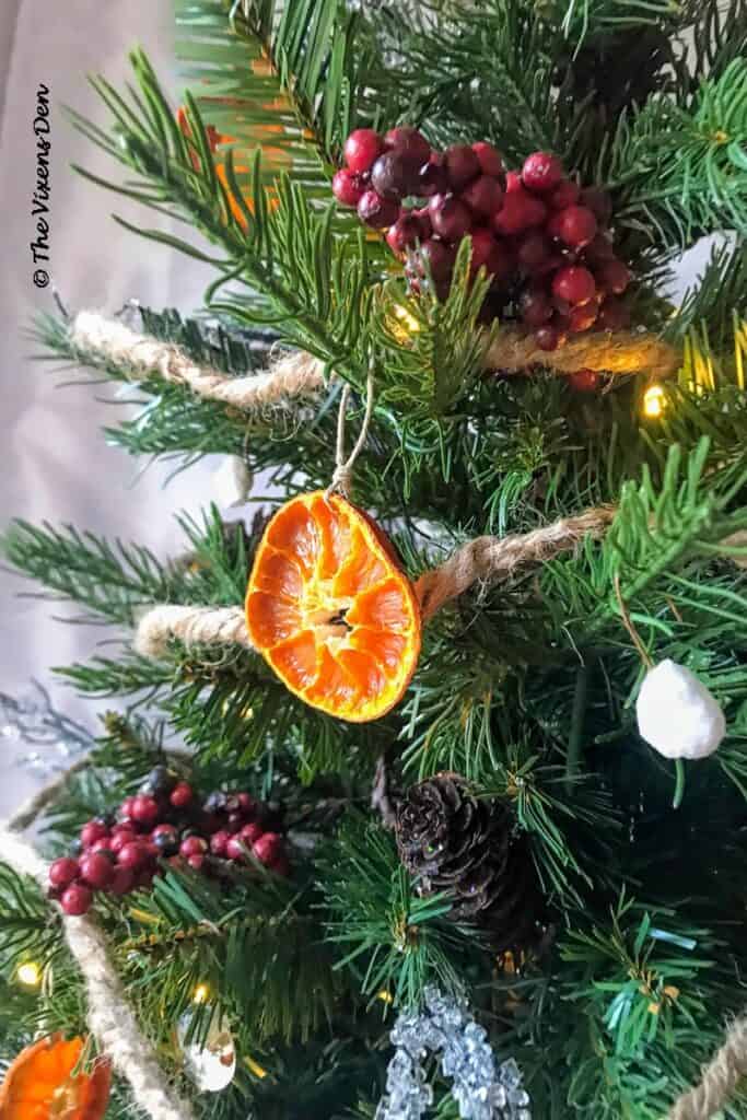 closeup showing DIY dried orange slices on a mini Christmas tree decorated with pinecones, berries, DIY rustic ornaments, and ice twigs