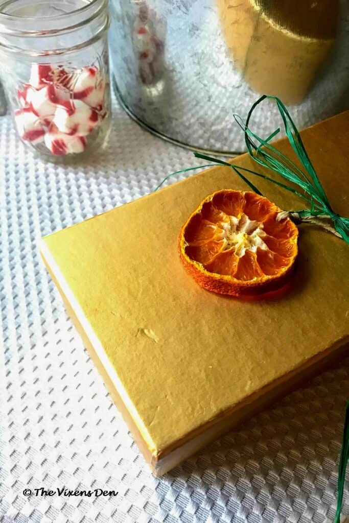 a gold box wrapped with green twine and embellished with a dried orange ornament, and a glass jar filled with peppermints