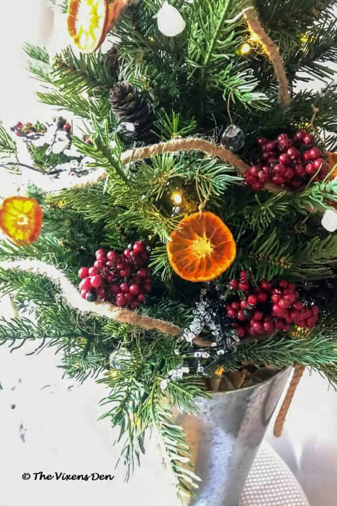 showing DIY dried orange slices on a mini Christmas tree decorated with pinecones, berries, DIY rustic ornaments, and ice twigs in a metal bucket