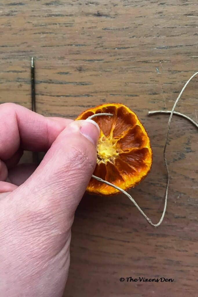 closeup showing the step of stringing a dried orange slice with hemp cord