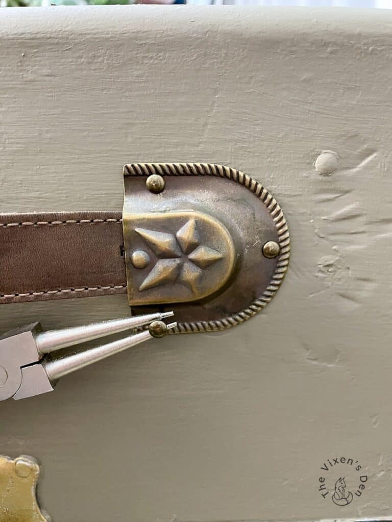 Old Wood Trunk Makeover-closeup of holding a small nail with pliers while replacing leather strap caps