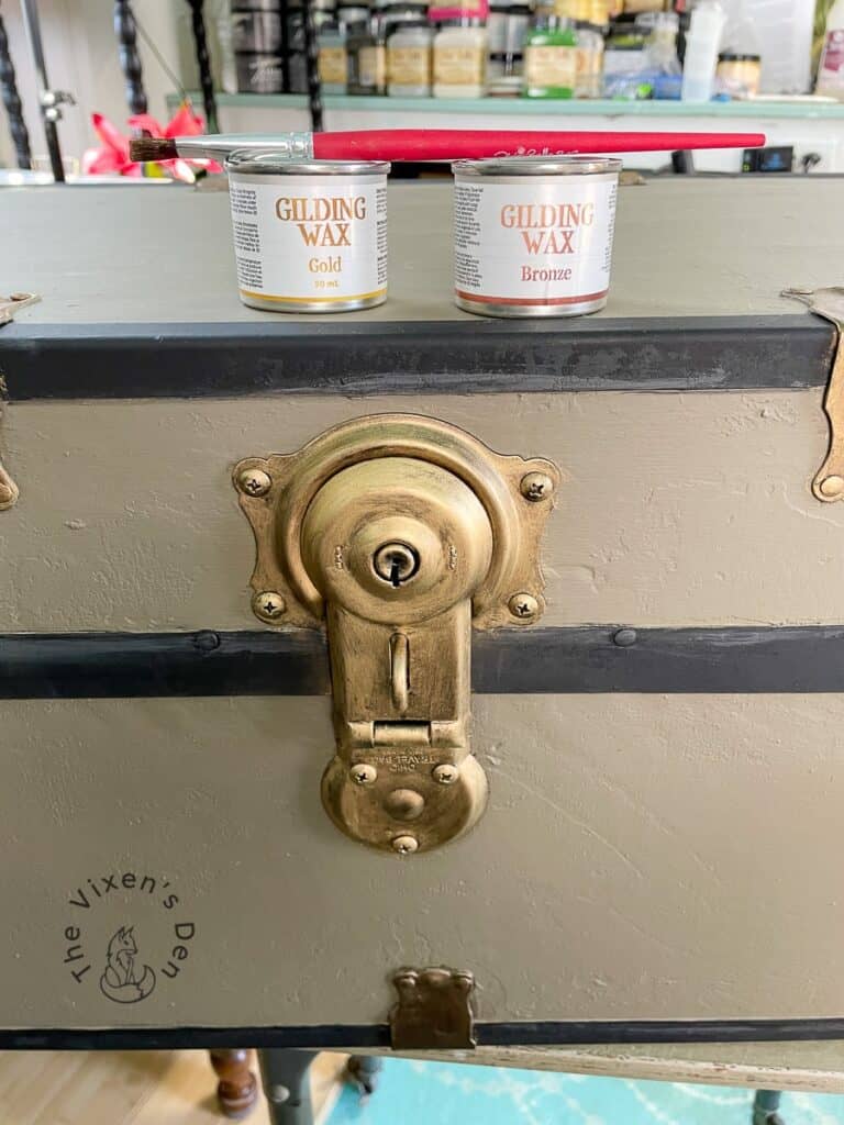 Old Wood Trunk Makeover-closeup of lock waxed with gold gilding wax and pots of gold and bronze wax sitting on top with a paintbrush