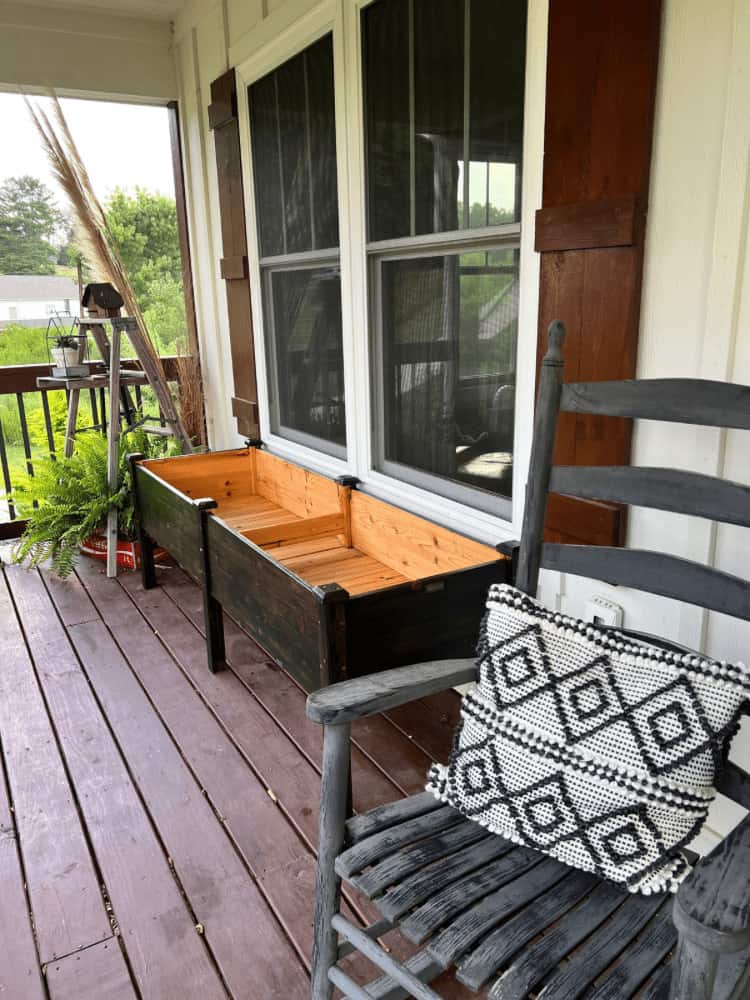 A rocking chair on a porch with a window box.