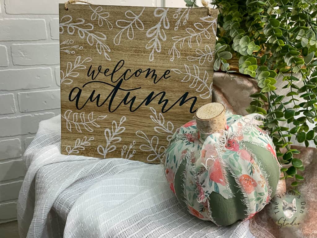 Green pumpkin with a sign and a plant on a table.