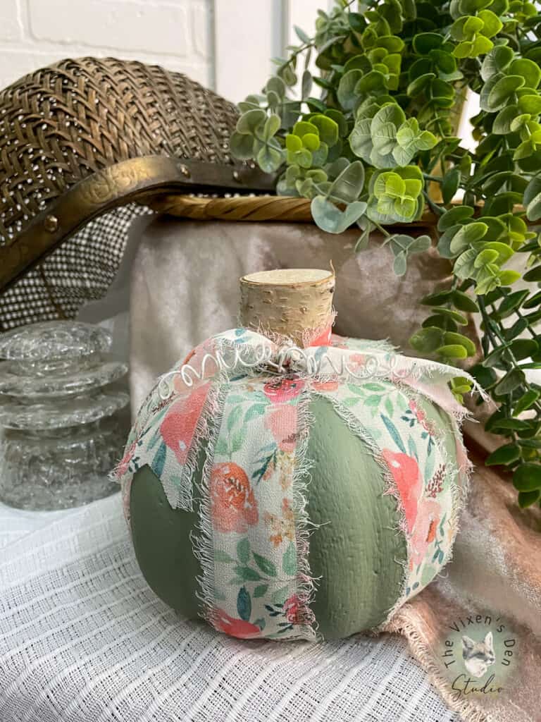 A green pumpkin on a table with a plant.