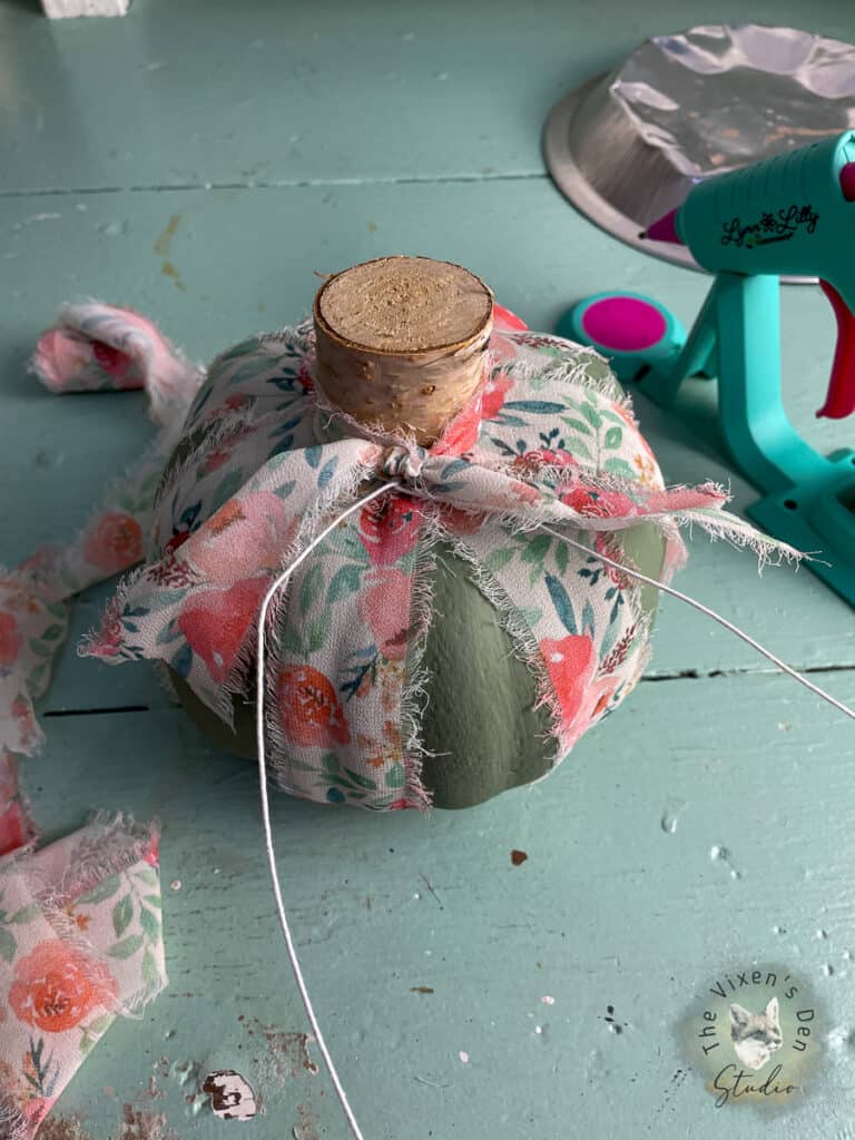 A green pumpkin on a table next to a glue gun.