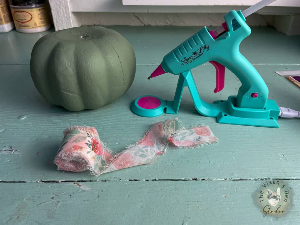 A glue gun and a pumpkin on a table.