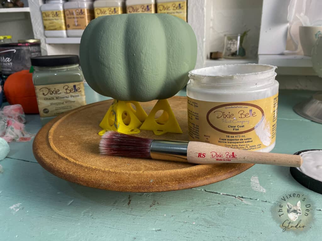 A pumpkin on a table next to a brush and paint.