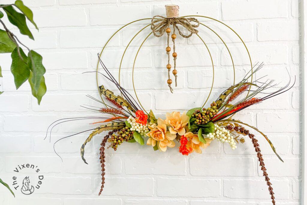 A pumpkin wreath with feathers hanging on a brick wall.