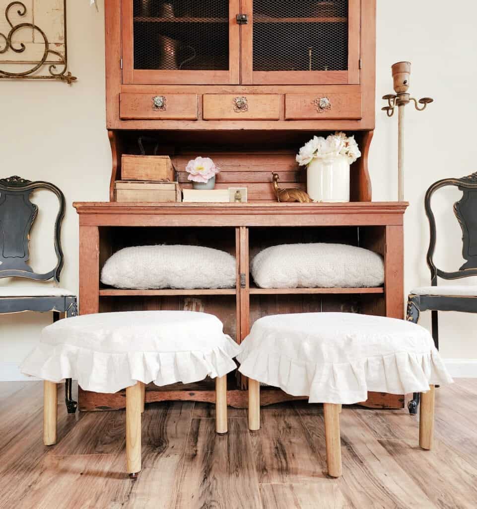 Two stools with ruffled skirts in front of a hutch.