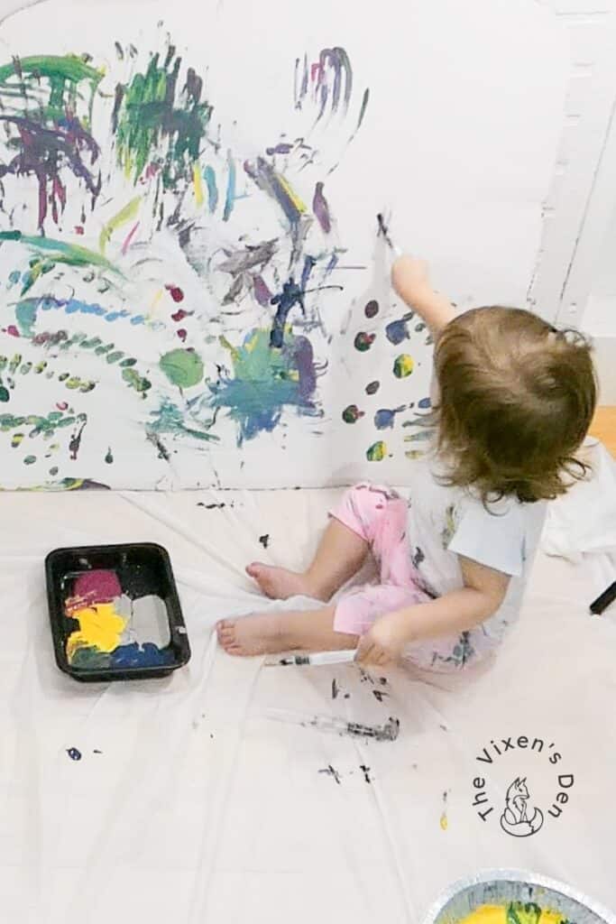 A baby is playing with paint on a white sheet.