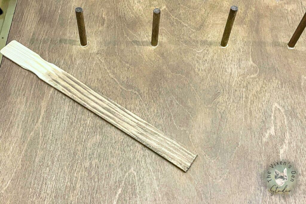 A wooden stick with stain on a board with pegs.