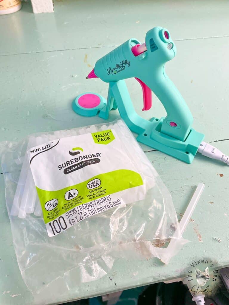 A glue gun and a plastic bag of glue sticks on a table.