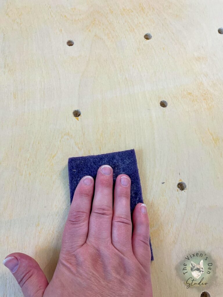 A person's hand is holding a sanding sponge on a wooden table.