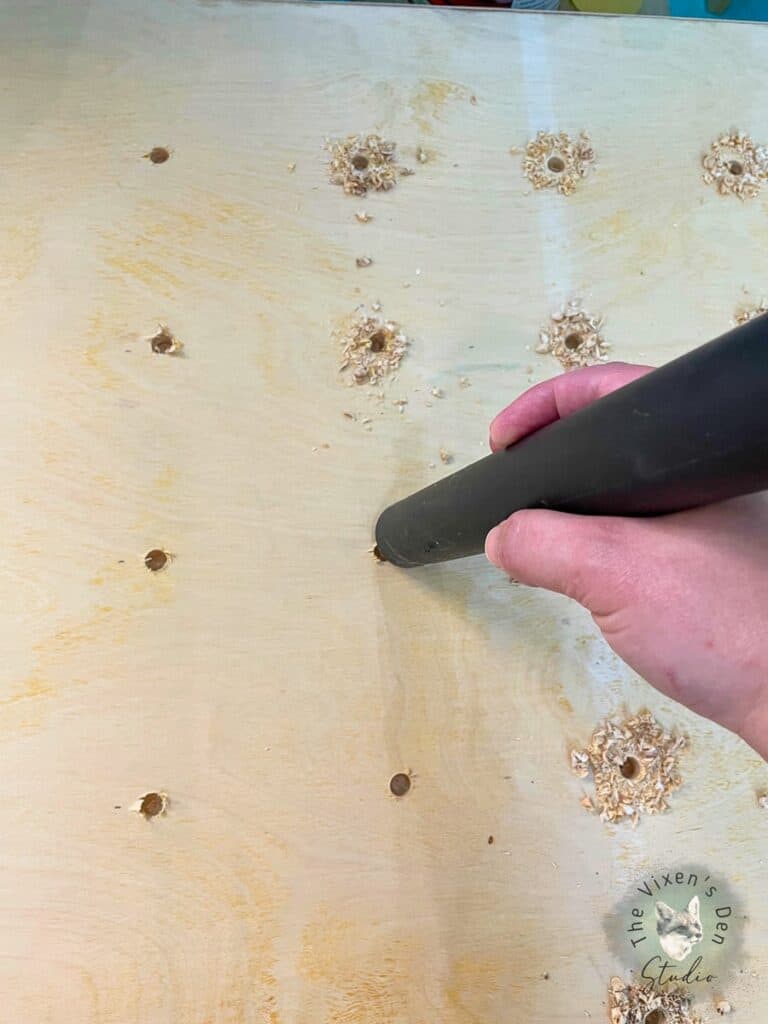 A person using a vacuum to clean out holes in a piece of wood.