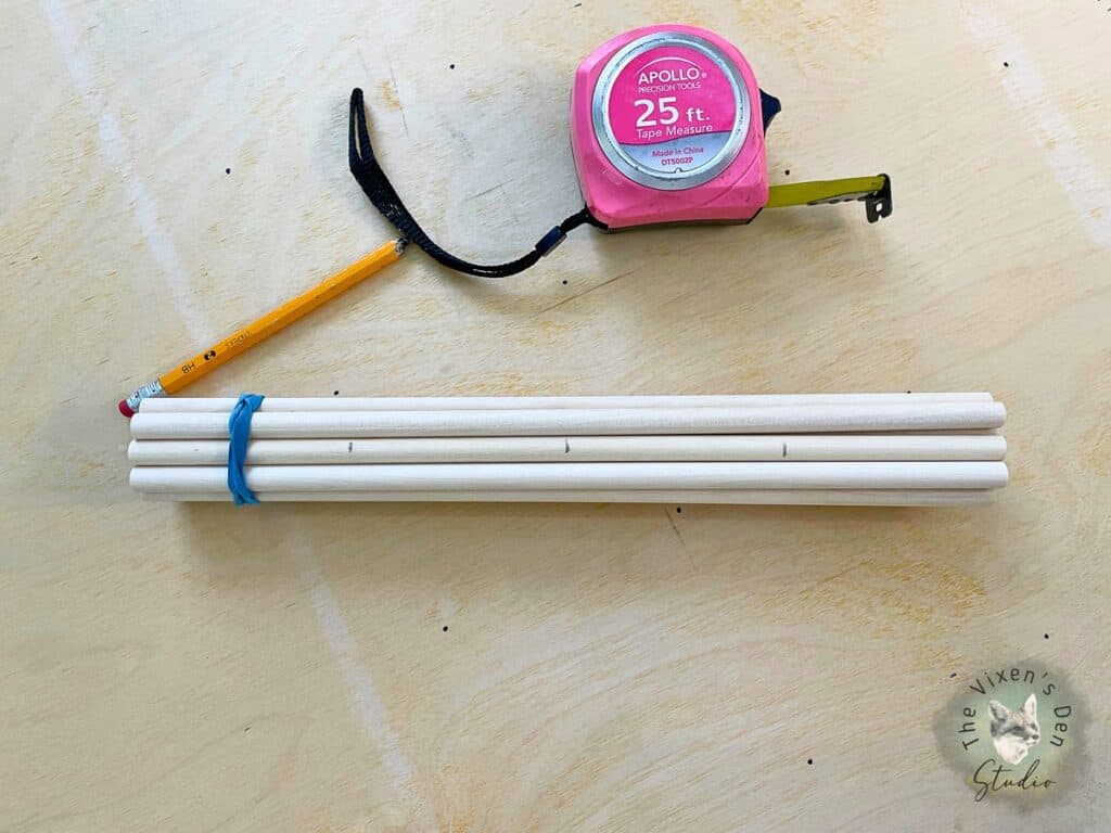 A pink tape measure next to a bundle of wooden dowels.