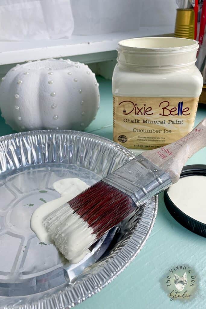 A paint brush next to a jar of paint on a table.