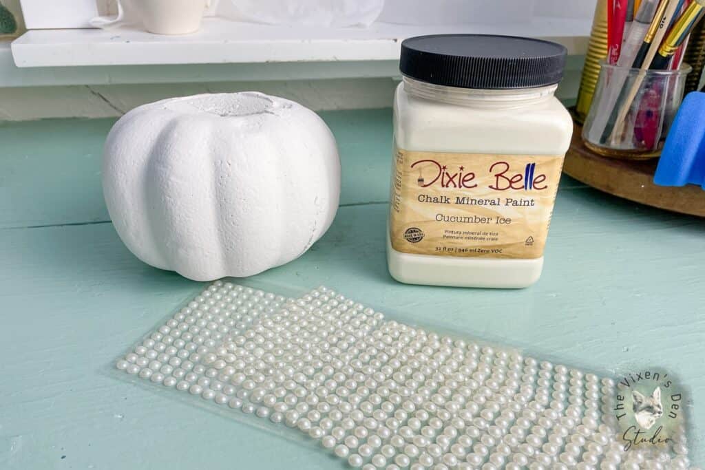 A white pumpkin next to a jar of pearls.