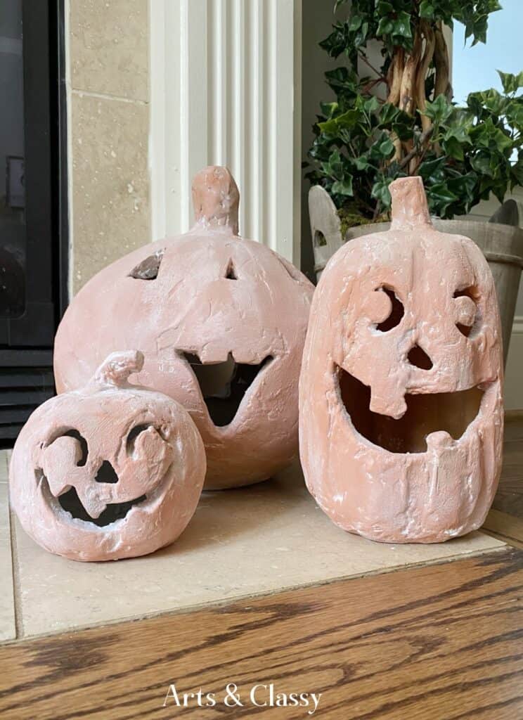 Three carved pumpkins sitting on a mantle in front of a fireplace.
