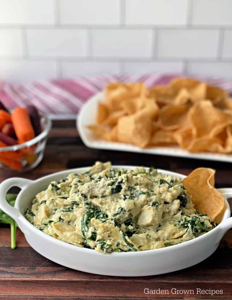 A bowl of spinach dip with chips and carrots.