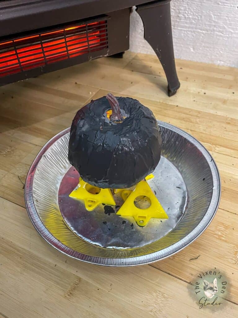 A black pumpkin sitting on a plate in front of a stove.