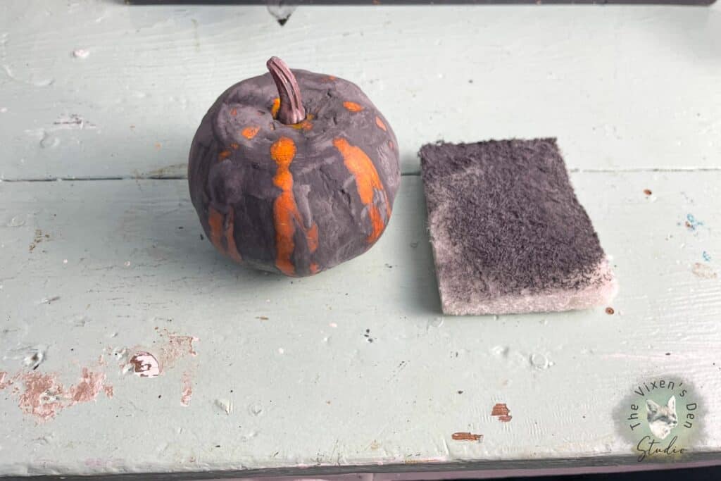 A pumpkin on a table next to a sponge.