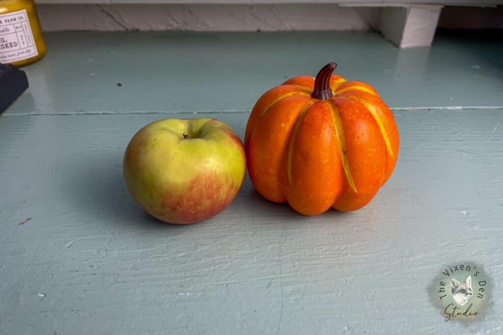 A pumpkin and an apple on a table.