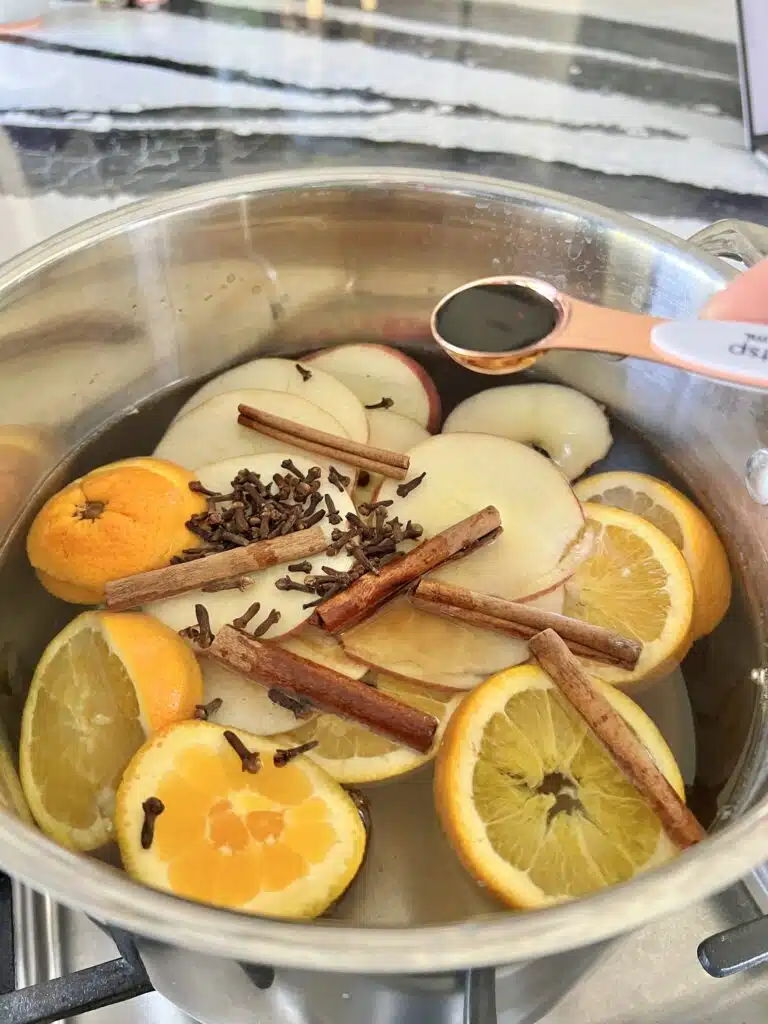 A pot with cinnamon sticks, apples and oranges in it.