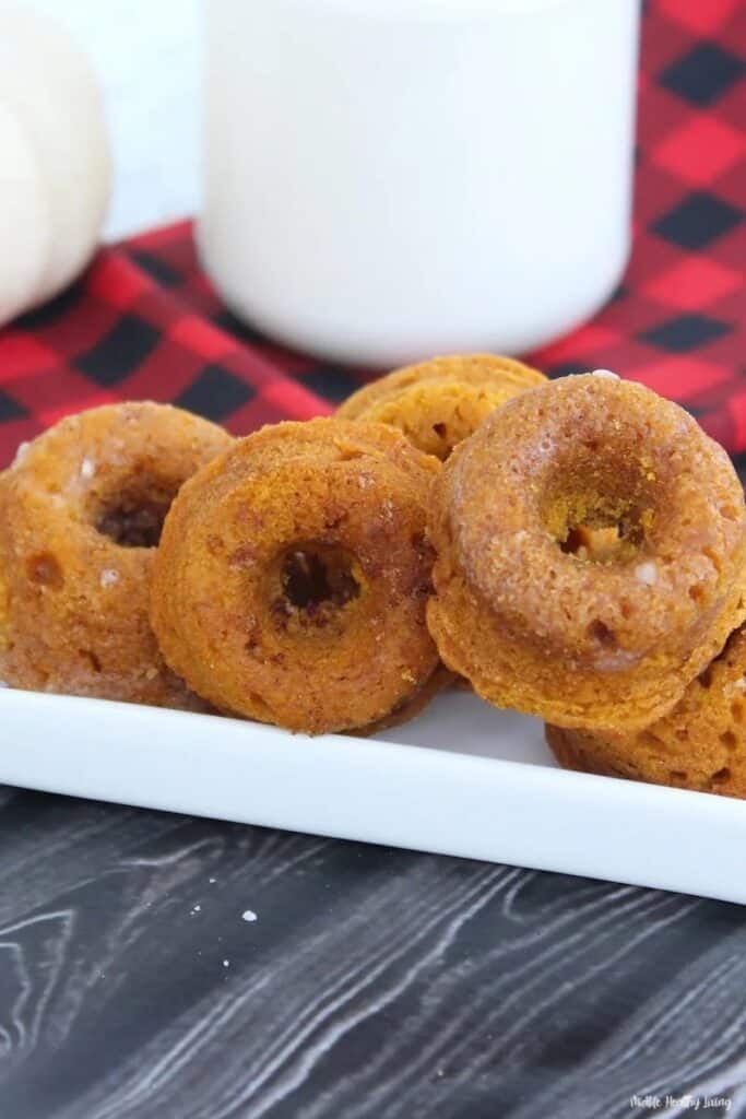 Pumpkin donuts on a white plate next to a glass of milk.