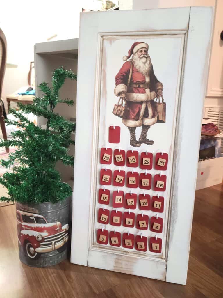 A santa claus advent calendar on a table next to a potted plant.