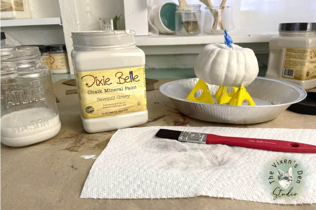 A pumpkin with paint and a brush on a table.