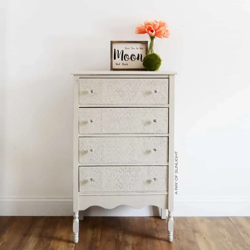 A white dresser with a flower on top.