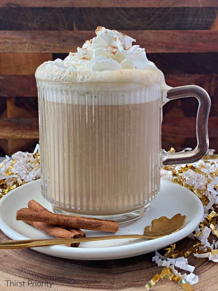 A cup of eggnog latte with whipped cream and cinnamon sticks.