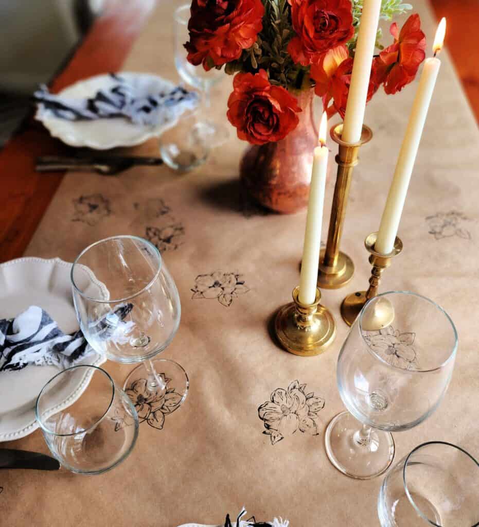A table setting with flowers and candles on a brown paper runner.