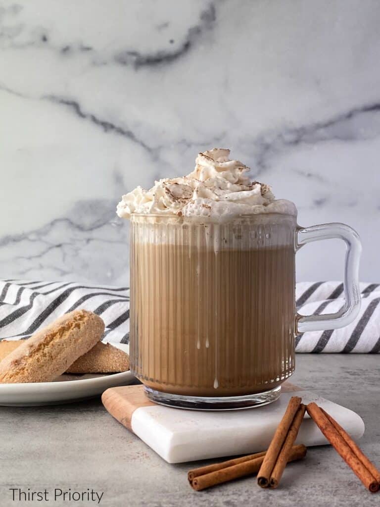 A cup of coffee with whipped cream and cinnamon sticks.