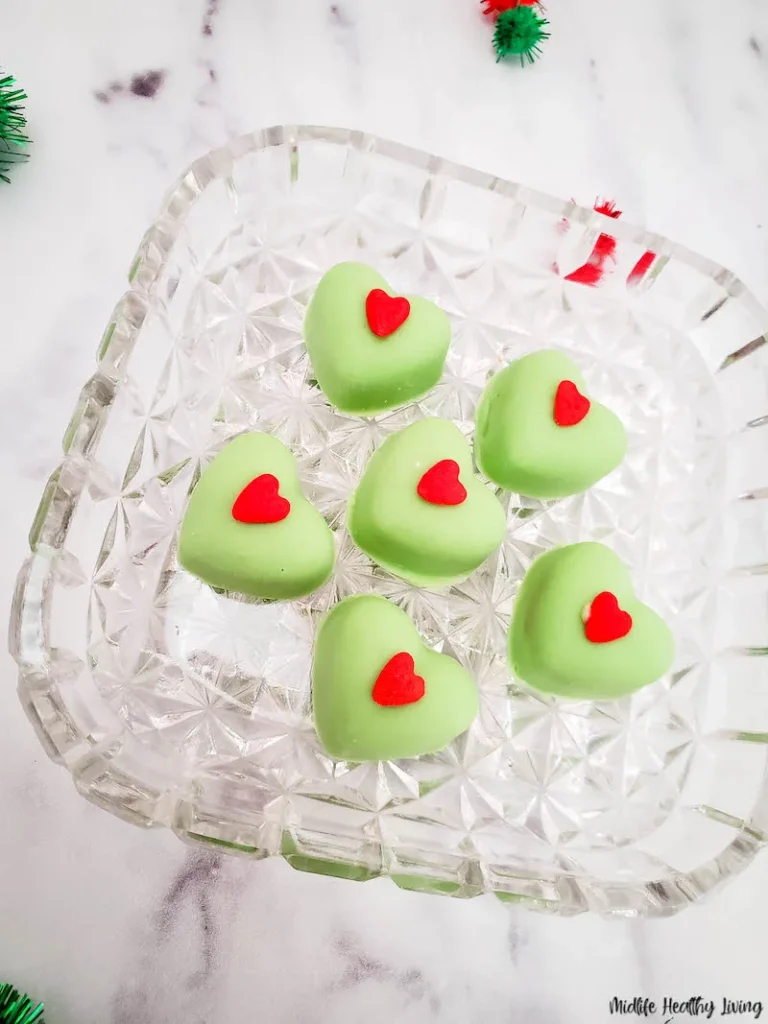 Five green heart shaped chocolates on a glass plate.