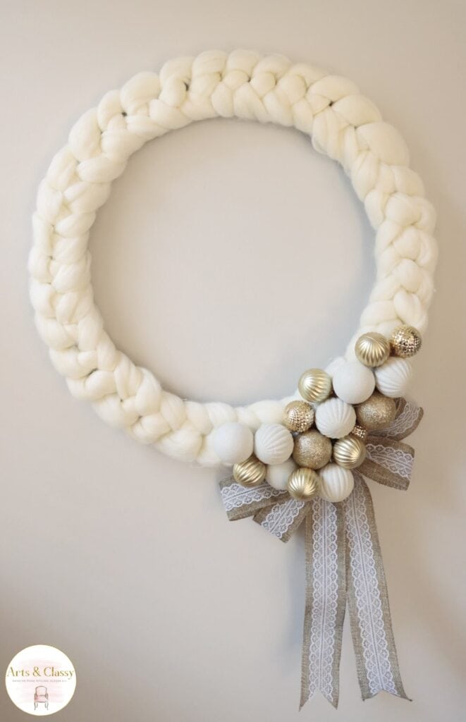 A white and gold knitted wreath hanging on a wall.