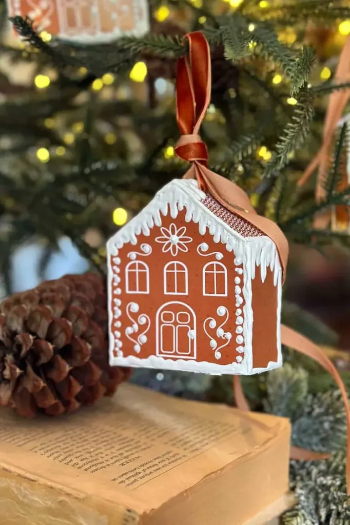 Gingerbread house ornament hanging on a christmas tree.