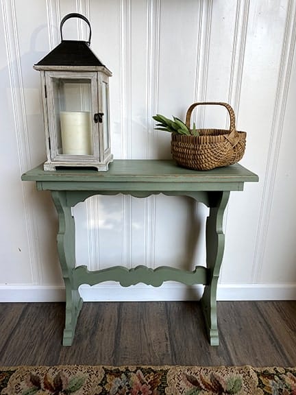 A green console table with a basket and lantern.