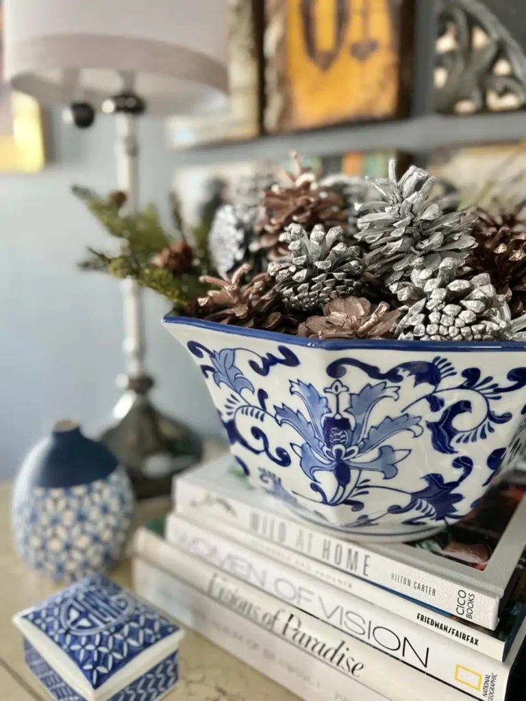 A blue and white bowl with pine cones on top of books.