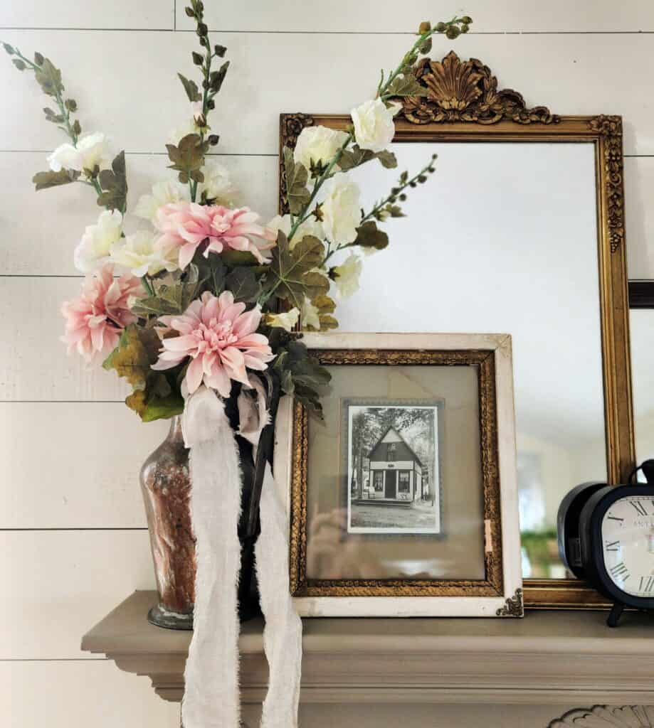 A mantle with a clock, flowers and a clock.