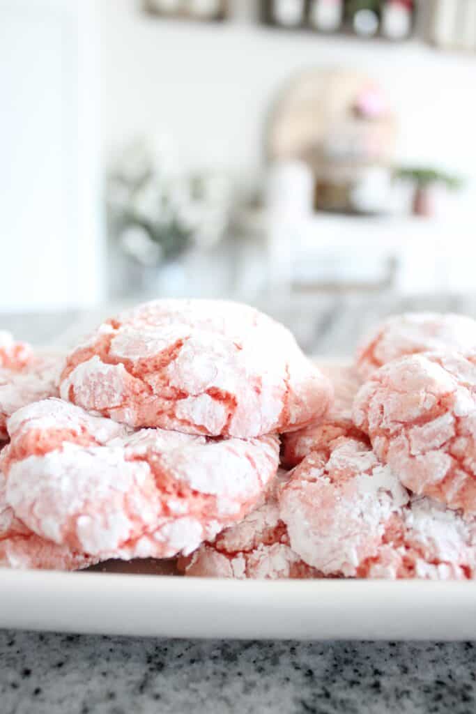 Pink powdered sugar crinkle cookies on a white plate.