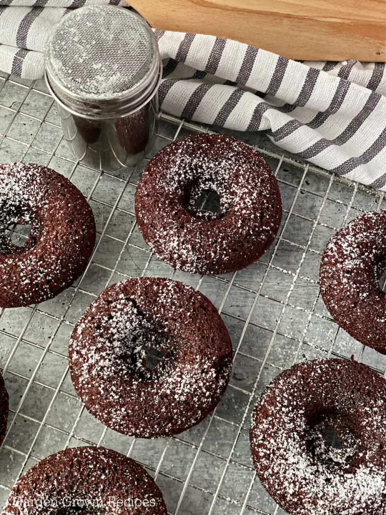 Chocolate donuts on a cooling rack with powdered sugar.