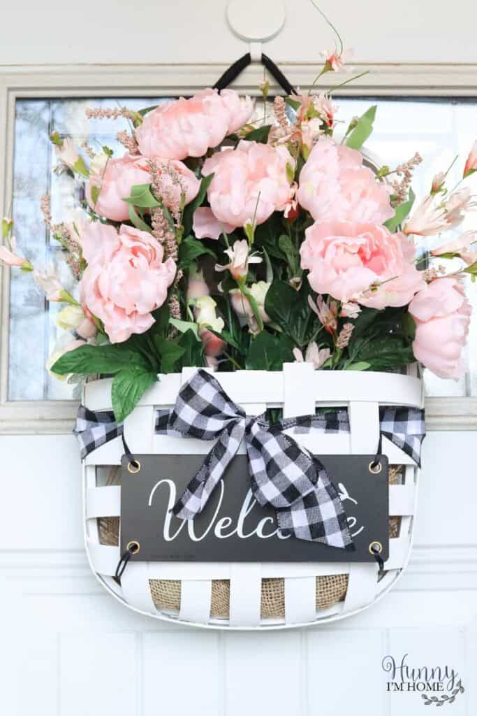 A basket with pink flowers and a welcome sign hanging on the front door.
