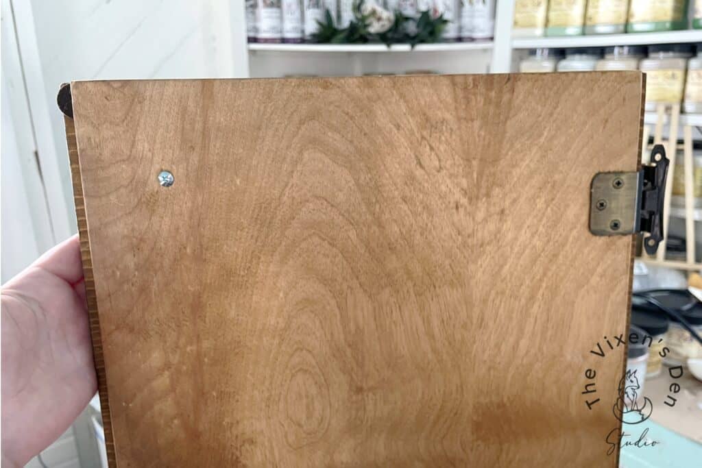 A wooden board with a metal hinge and a visible screw, possibly a part of furniture or fixture.