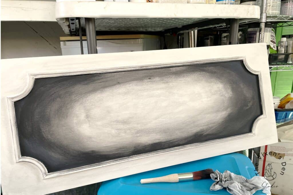 Chalkboard paint applied on wooden frame with brush and cloth on a workshop table.